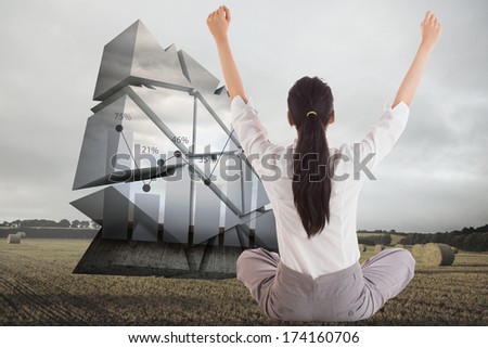 Businesswoman sitting cross legged cheering against landscape with bales of straw