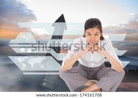 Smiling businesswoman sitting cross legged against road turning into arrow