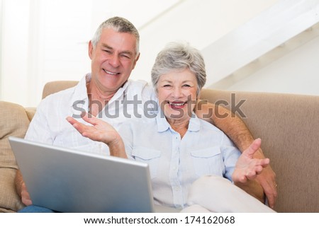 Portrait of happy senior couple with laptop on sofa