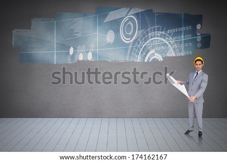 Serious architect with hard hat holding plans against display on wall showing technology interface