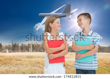 Smiling brother and sister holding their exercise books against large city on the horizon