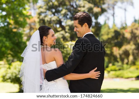 Rear view of a newlywed couple with arms around standing in the park