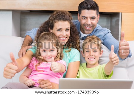 Happy family sitting on sofa using laptop giving thumbs up at home in living room