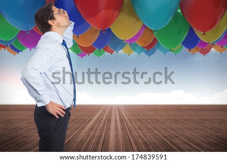 Thinking businessman tilting glasses against many colourful balloons sky background
