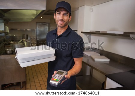 Smiling pizza delivery man holding credit card machine in a commercial kitchen