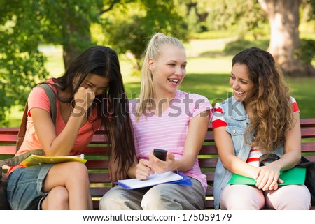 Group portrait of happy female college friends sitting on bench at the campus