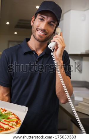 Happy pizza delivery man taking an order over the phone in a commercial kitchen