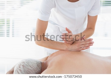 Female physiotherapist massaging back of senior man in clinic