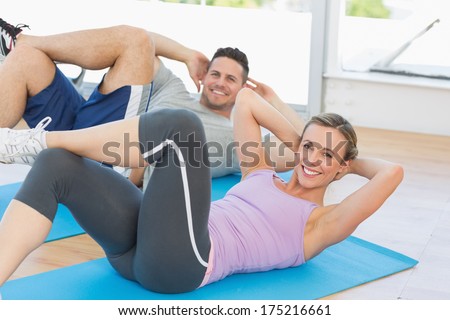 Portrait of fit woman and man doing sits up in fitness studio