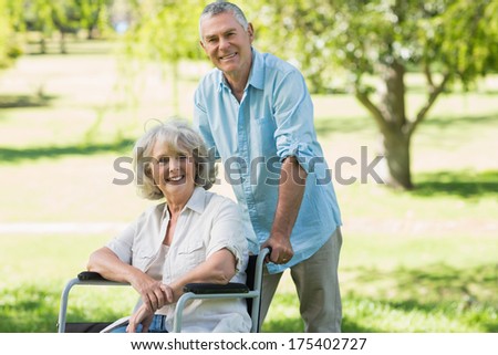 Portrait of a smiling mature man with woman sitting in wheel chair at the park