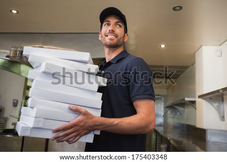 Smiling pizza delivery man holding many pizza boxes in a commercial kitchen