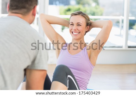 Male trainer assisting fit woman in doing sits up in exercise room
