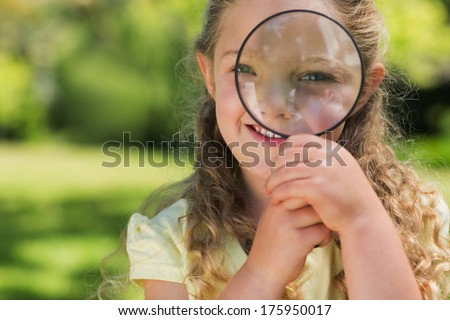 Close-up portrait of a cute young girl looking through magnifying glass at the park