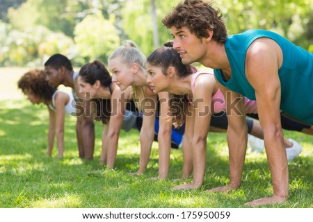 Side View Of A Group Of Fitness People Doing Push Ups In The Park