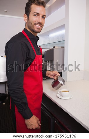 Happy barista pouring milk into cup of coffee in a cafe