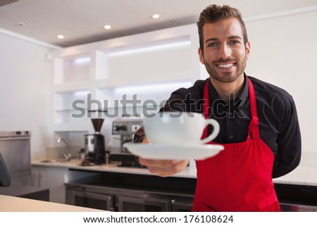 Happy Barista Offering Cup Of Coffee To Camera In A Cafe