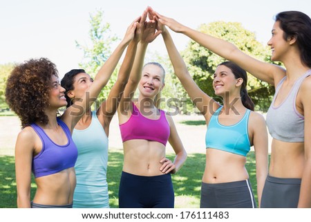 Happy young women in sportswear raising hands together in park