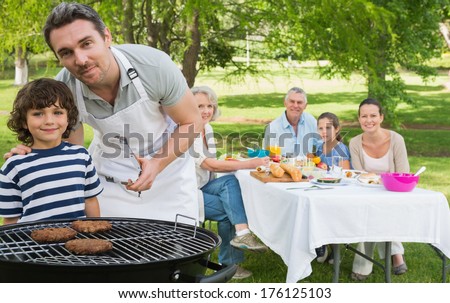 Father and son at barbecue grill with extended family having lunch in the park
