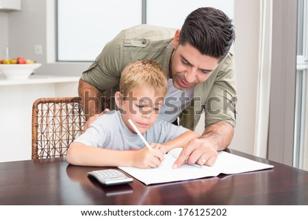 Happy father helping son with math homework at table at home in kitchen