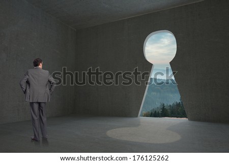 Businessman with hands on hips against keyhole door in dark room