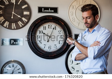 Handsome businessman checking the time at the local bar beside wall of international clocks