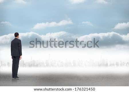 Businessman turning his back to camera against city on the horizon