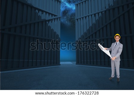 Serious architect with hard hat holding plans against door opening in dark room