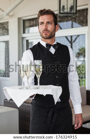 Handsome waiter holding tray of champagne in the patio of restaurant