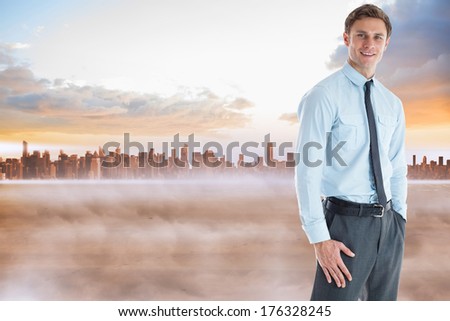 Smiling businessman standing with hand in pocket against cityscape on the horizon