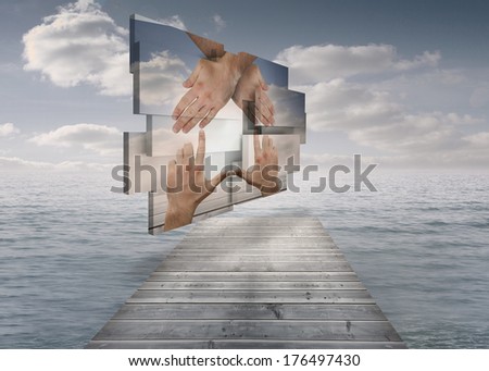 Hands making a house on abstract screen against bridge in ocean under cloudy sky