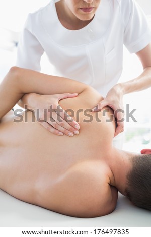 Professional female therapist giving shoulder massage to man in hospital