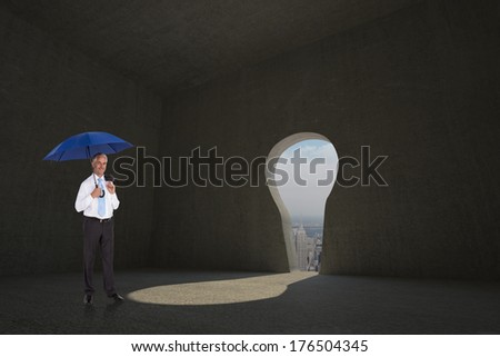 Happy businessman holding umbrella against keyhole door in dark room