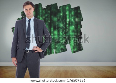 Serious businessman with hand on hip against display on wall showing green matrix