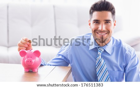 Happy businessman putting coins into piggy bank in the office