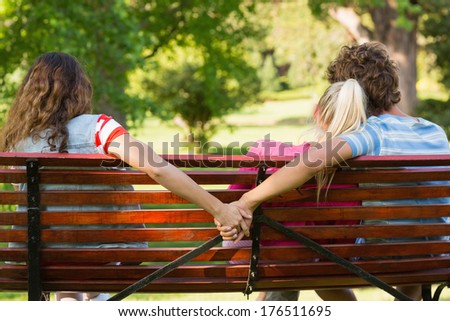 Rear view of a man with girlfriend while holding hands with another woman in the park