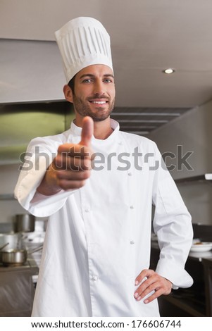 Happy young chef looking at camera showing thumb up in a commercial kitchen