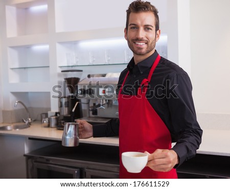 Handsome young barista holding jug and cup of coffee in a cafe