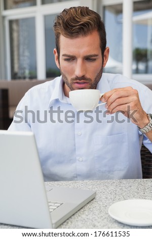 Handsome businessman working with laptop drinking coffee in patio of restaurant