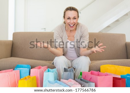 Excited woman looking at camera with many shopping bags at home in the living room