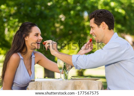Smiling young couple with champagne flutes feeding strawberries to each other at an outdoor cafÃ?Â©