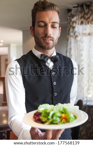 Waiter showing bowl of salad to camera in a fancy restaurant