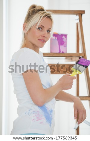 Portrait of a young woman holding paint brush in front of ladder at the new house