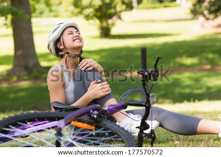 Young female bicyclist with hurt leg sitting on grass in the park