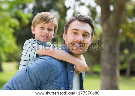 Side view portrait of a father carrying young boy on back at the park