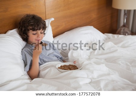 Smiling young boy eating breakfast in bed at home