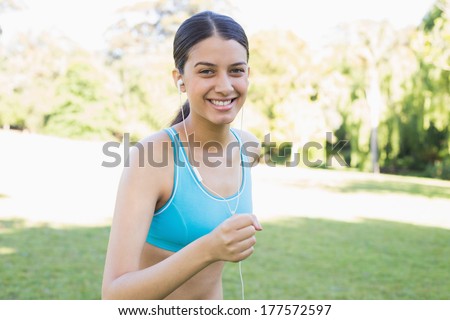 Portrait of happy female jogger listening music while running in park