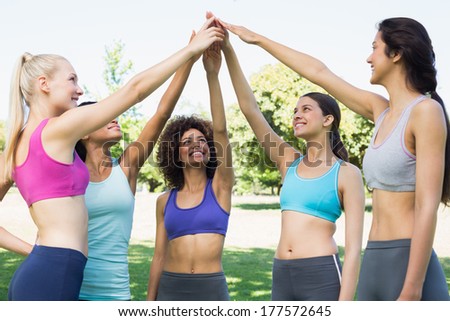 Happy young women in sportswear raising hands together in park
