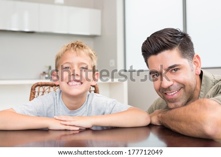 Father and son smiling at camera at the table at home in kitchen