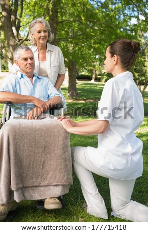 Two women with a mature man sitting in wheel chair at the park