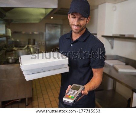 Happy pizza delivery man holding credit card machine in a commercial kitchen
